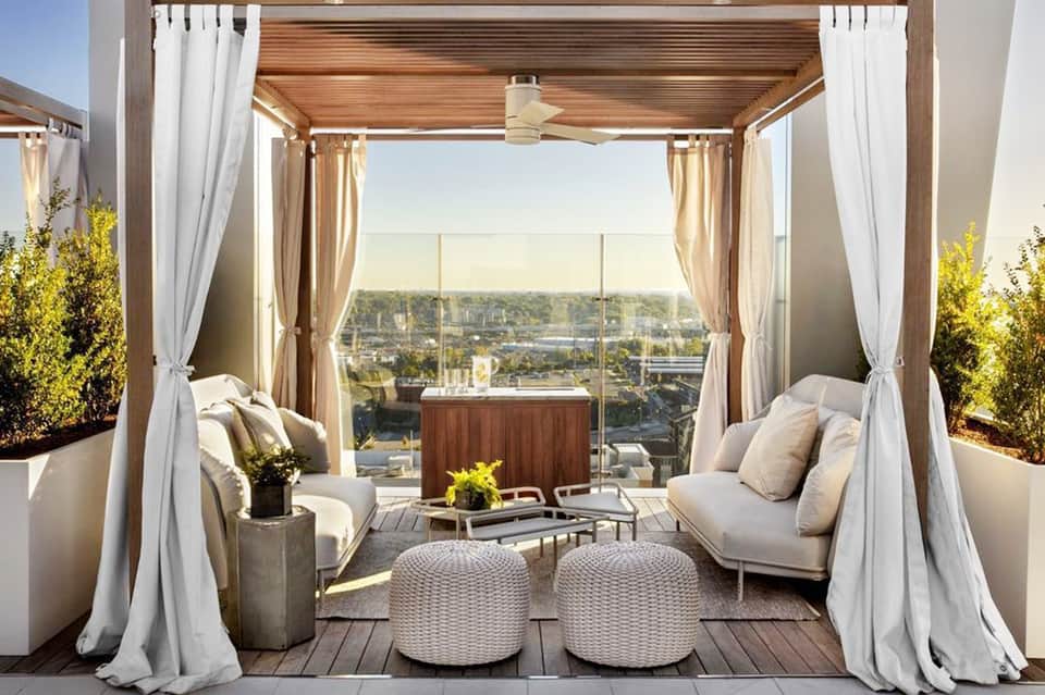 Elegant rooftop terrace with daybed pavilions, curtains, and panoramic city views across waterfront