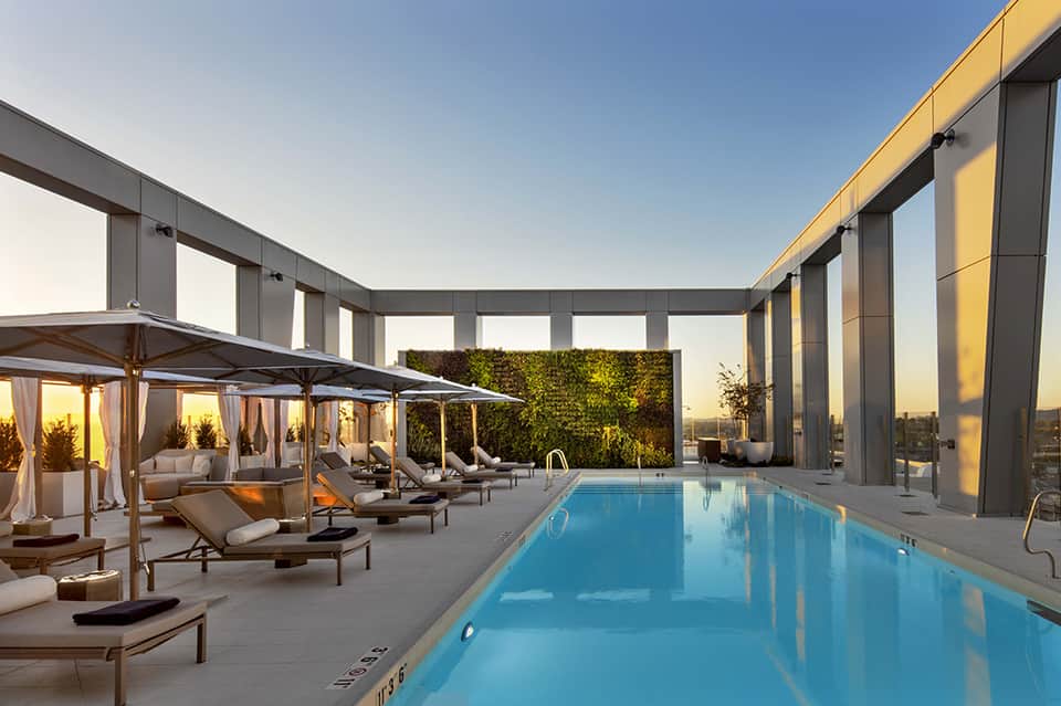 Indoor luxury pool with glass walls, lounge chairs with cabanas, and city skyline at sunset