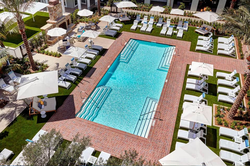 Aerial view of rectangular pool surrounded by white lounge chairs, umbrellas, and manicured green lawn