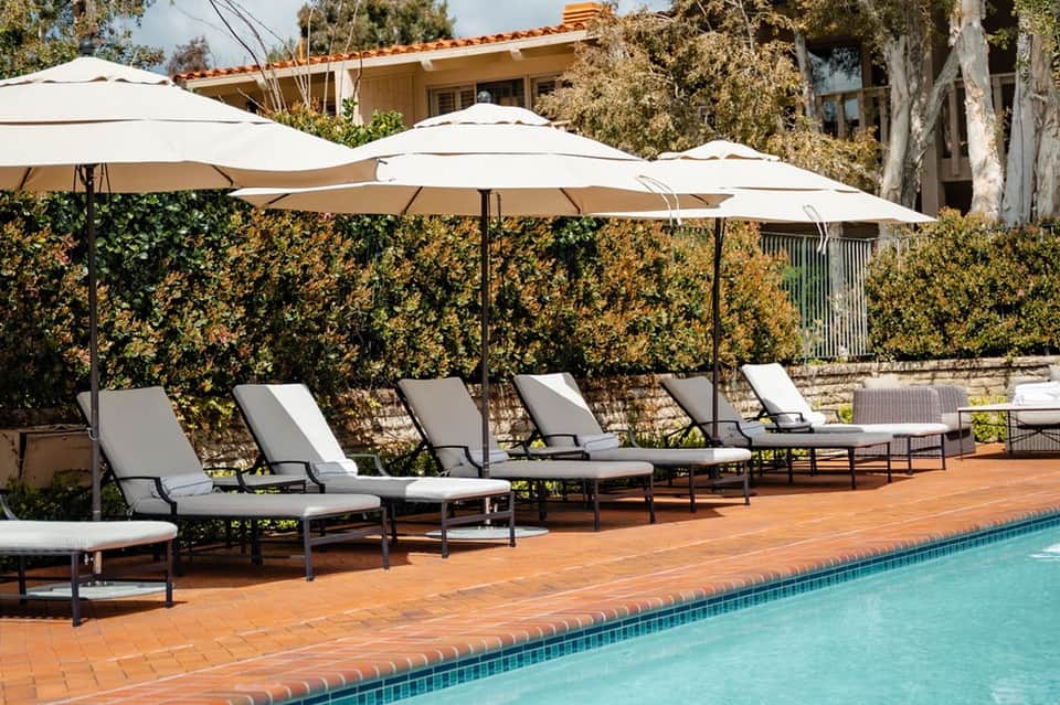 Lounge chairs with white cushions under large white umbrellas beside turquoise swimming pool
