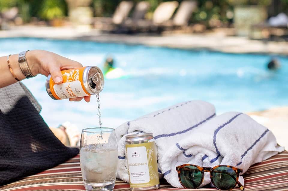 Woman pouring sparkling beverage by resort pool with lounge chairs and swimmers in background