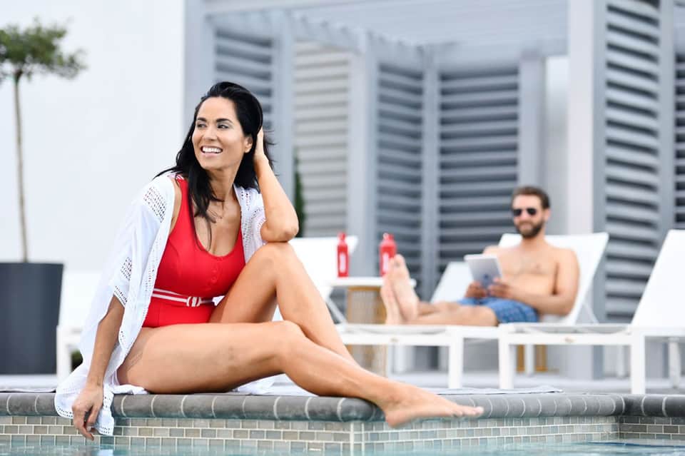 Woman in red swimwear relaxing by pool edge with modern high-rise buildings in background