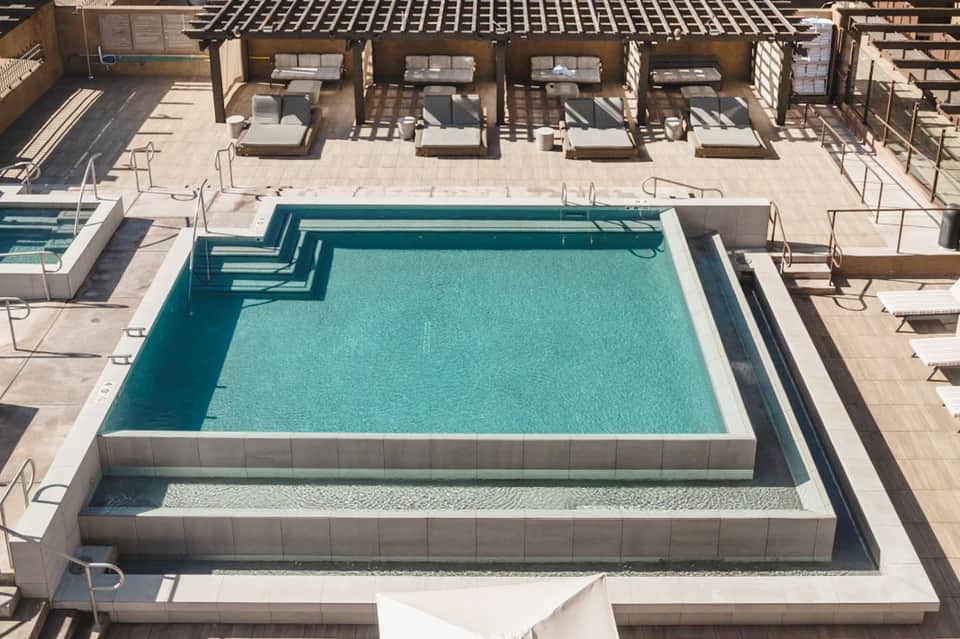 Aerial view of multi-level pool deck with lounge chairs, umbrellas, and modern architectural design