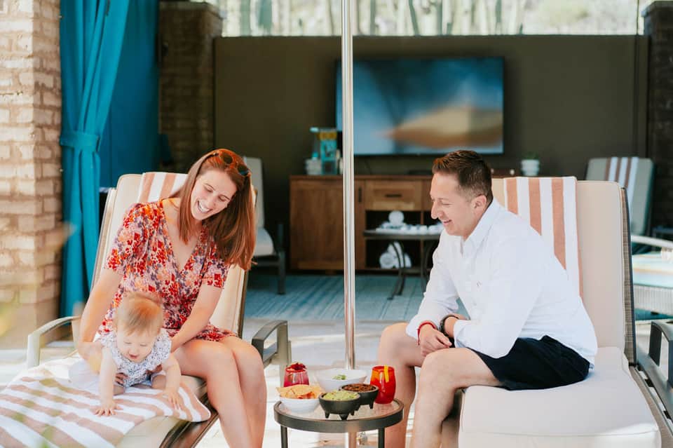 Family relaxing on balcony lounge chairs overlooking resort with drinks and snacks