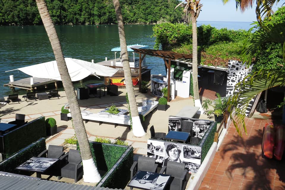 Beachfront lounge area with white cabanas, palm trees, and waterfront seating