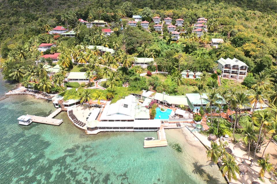 Aerial view of beachfront resort with pink-roofed bungalows nestled in tropical jungle by turquoise water