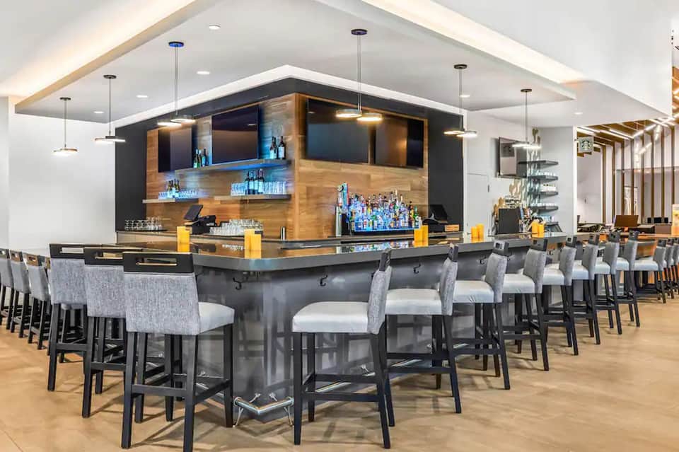 Contemporary hotel bar with modern black and wood design, seating, and illuminated bottles