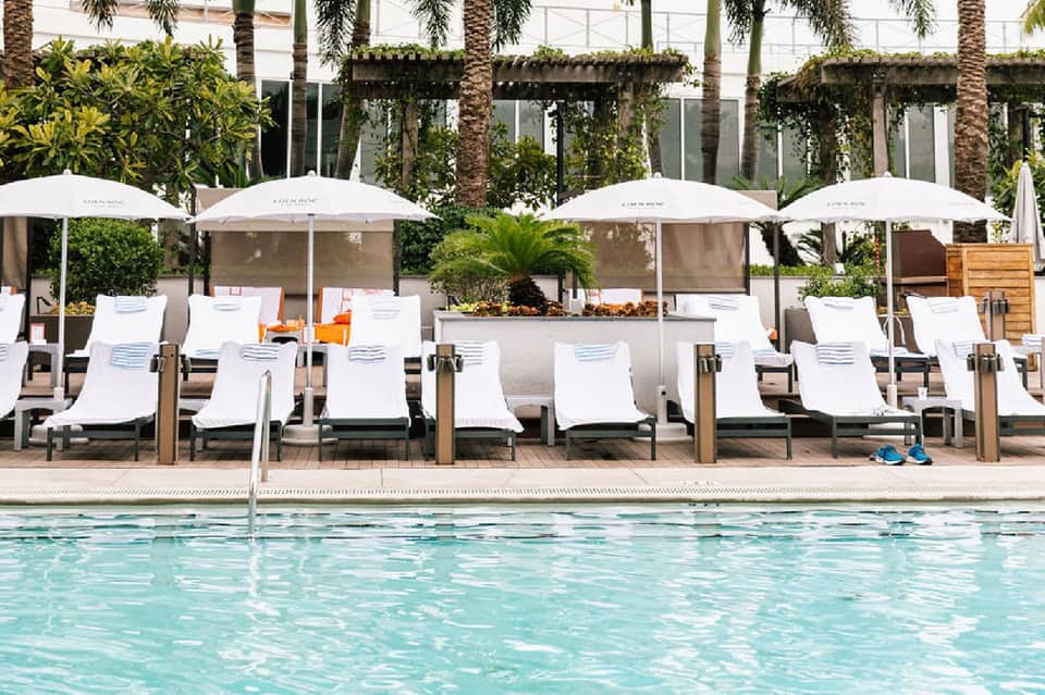 Resort poolside lounge area with white umbrellas, sun loungers, and modern architecture