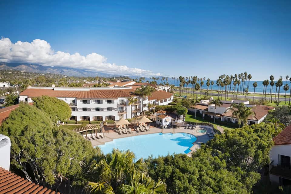 Coastal resort with curved pool, white buildings, palm trees, and ocean view