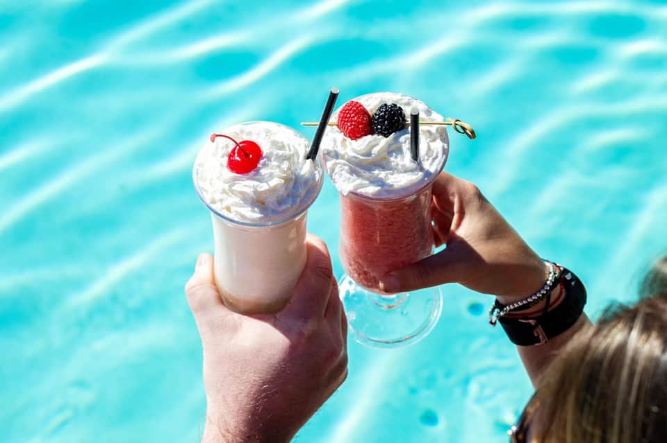 Two colorful frozen drinks with whipped cream and berries held poolside