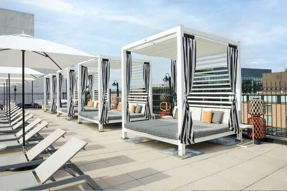 Rooftop lounge with white cabanas, striped curtains, white umbrellas, and city skyline views