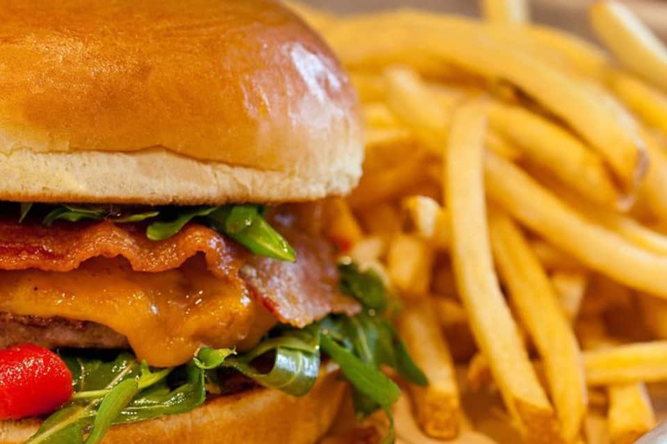 Close-up of gourmet burger with crispy bacon, cheese, greens, and golden French fries