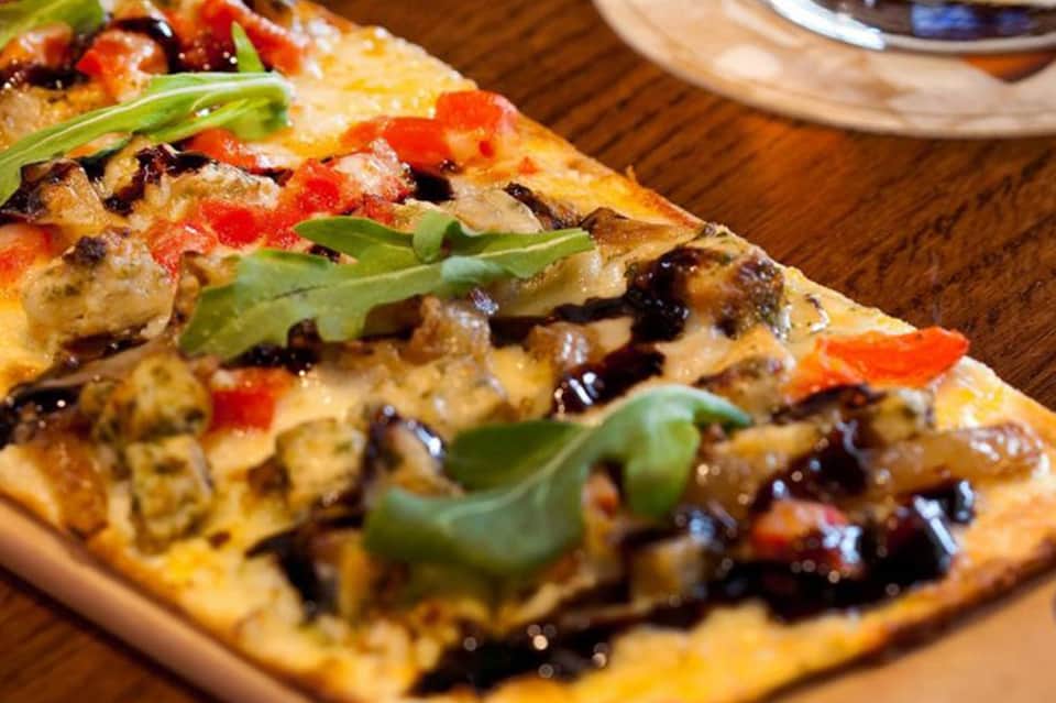 Gourmet pizza with cheese, vegetables, and fresh basil on wooden serving board