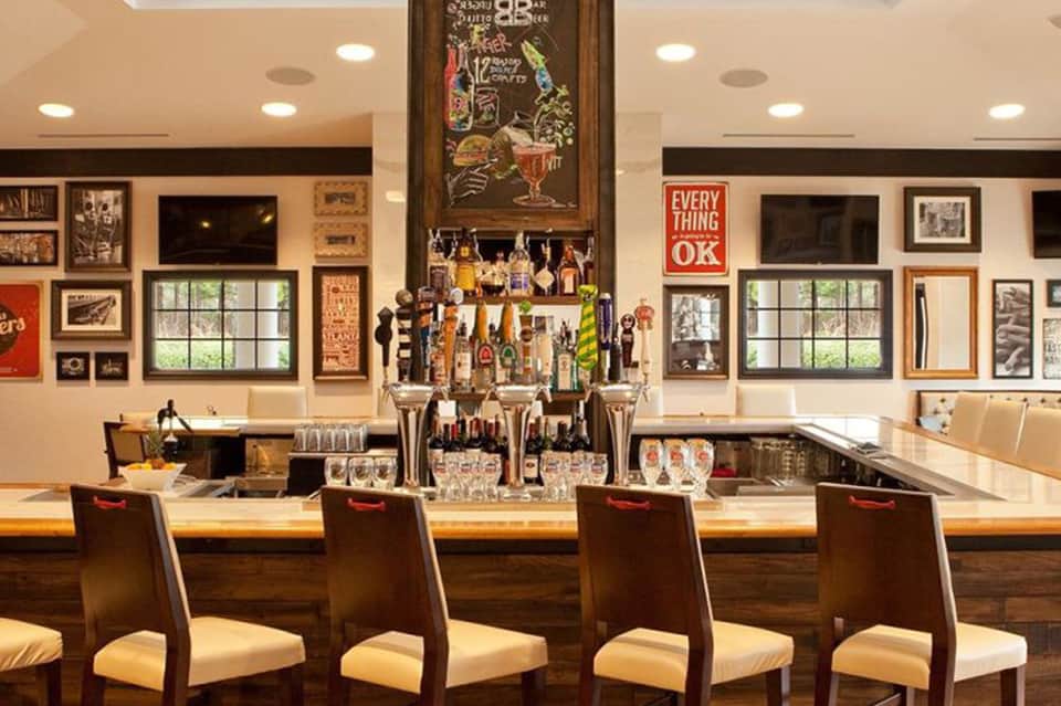Hotel bar with vintage decor, framed photographs, bottles, and seating for guests