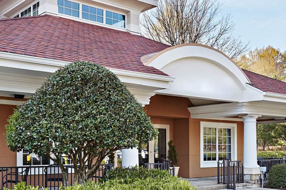 Elegant colonial-style building entrance with burgundy roof, white columns, and manicured landscaping