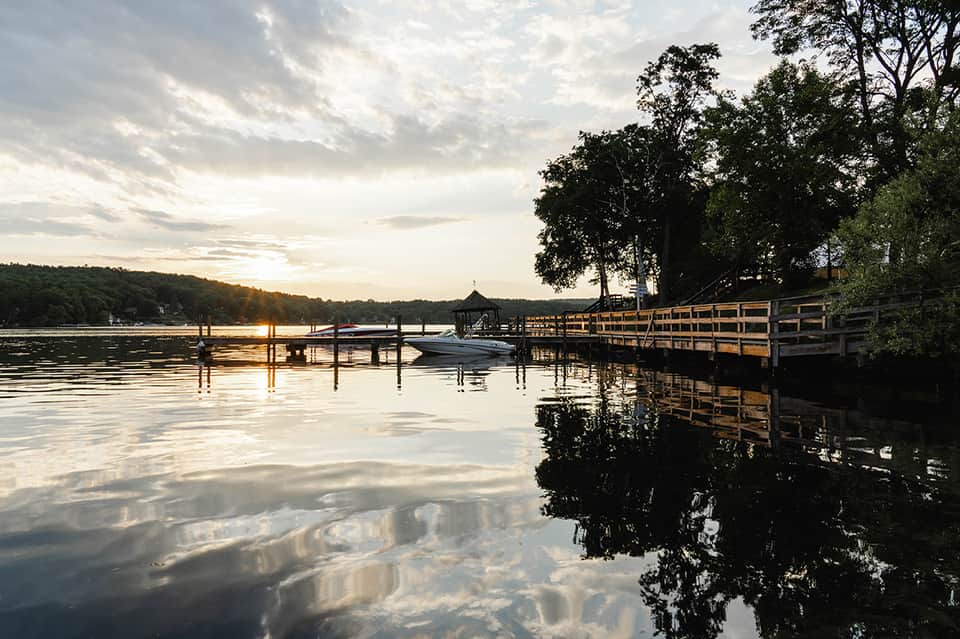 Lakeside dock at dusk with boat, wooden pier, and tree-lined shoreline