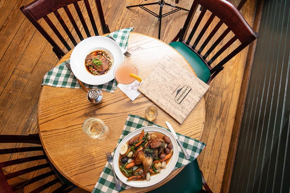 Overhead view of dining table with gourmet plated dishes, beverage, and green gingham napkins on wood surface