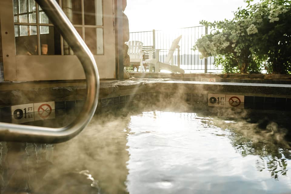 Steaming hot spring pool with depth markers and viewing area overlooking landscaped grounds