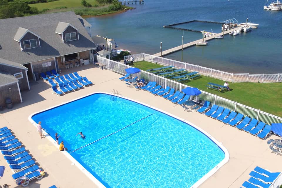 Aerial view of resort pool with blue lounge chairs, marina, and waterfront houses