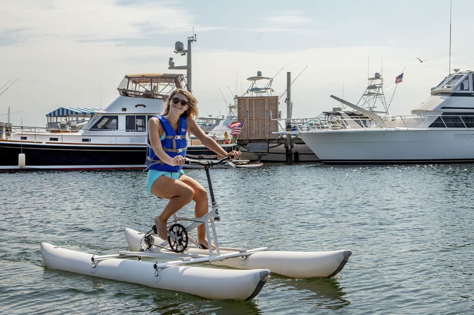 Woman on paddleboard with scooter in marina surrounded by boats