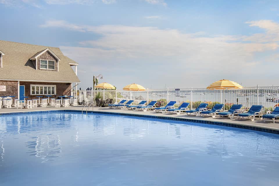 Residential-style pool area with blue lounge chairs, yellow umbrellas, white fence, and waterfront views
