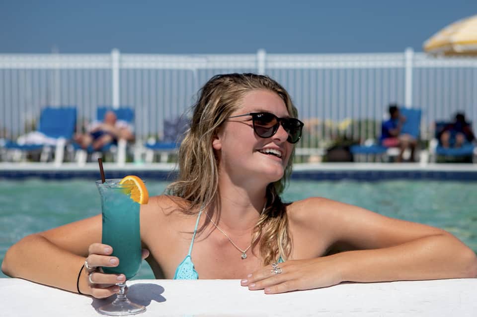 Woman in turquoise bikini enjoying a blue cocktail while relaxing in a resort pool