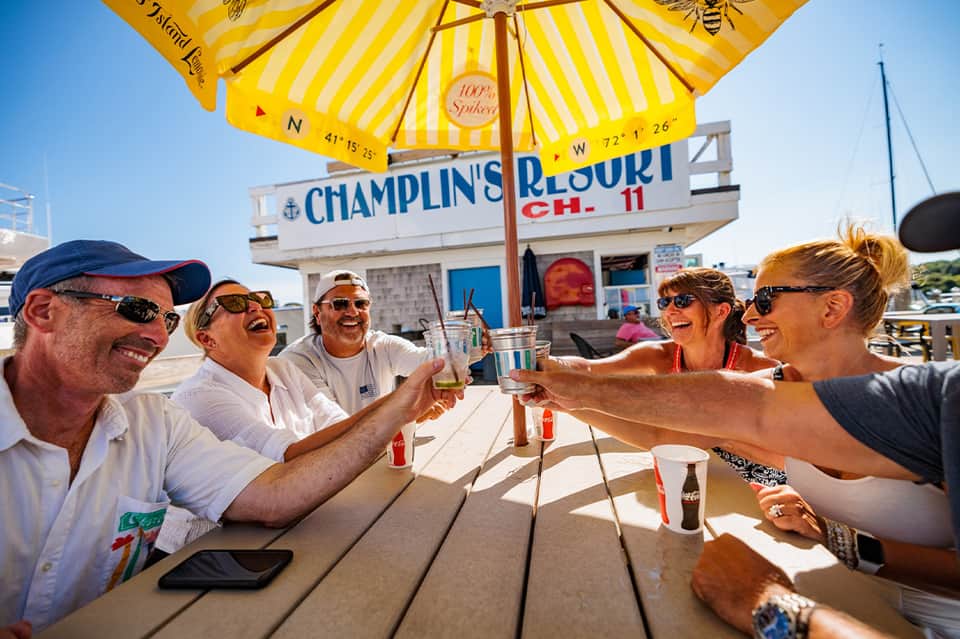 Group of people toasting drinks at outdoor waterfront restaurant under yellow umbrella