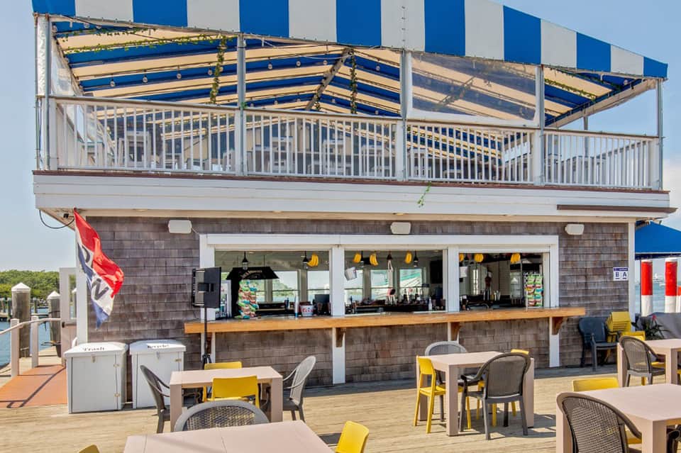 Waterfront restaurant deck with blue and white striped awning, bar, and yellow accent seating