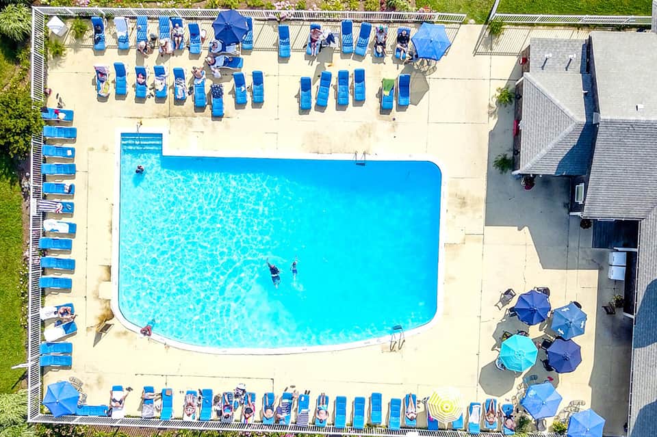 Aerial view of curved resort pool with blue lounge chairs, sandy deck, and surrounding buildings