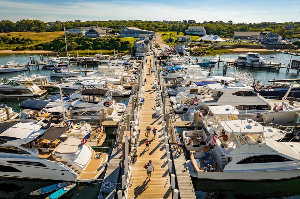 Aerial view of busy marina with wooden dock, boats, and waterfront homes