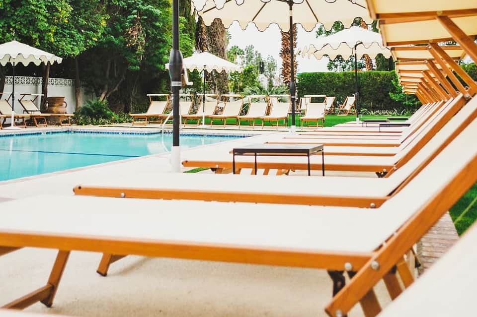 Poolside lounge area with orange and white wooden chairs, white umbrellas, and manicured gardens