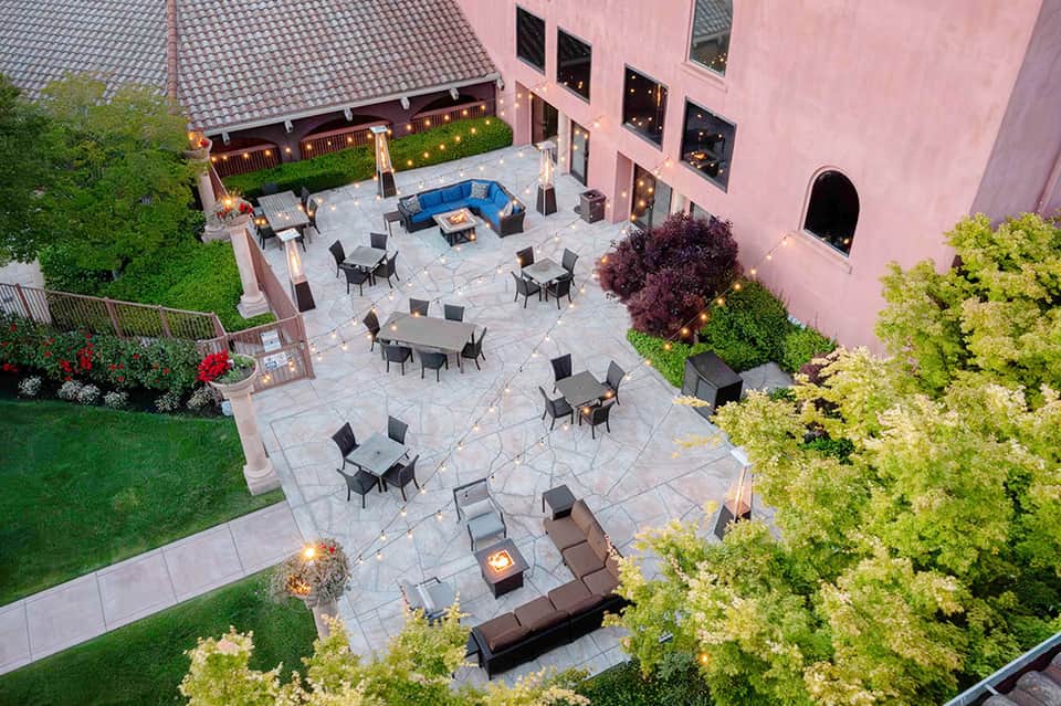 Aerial view of pink building courtyard with blue seating area, fire pit, and manicured gardens