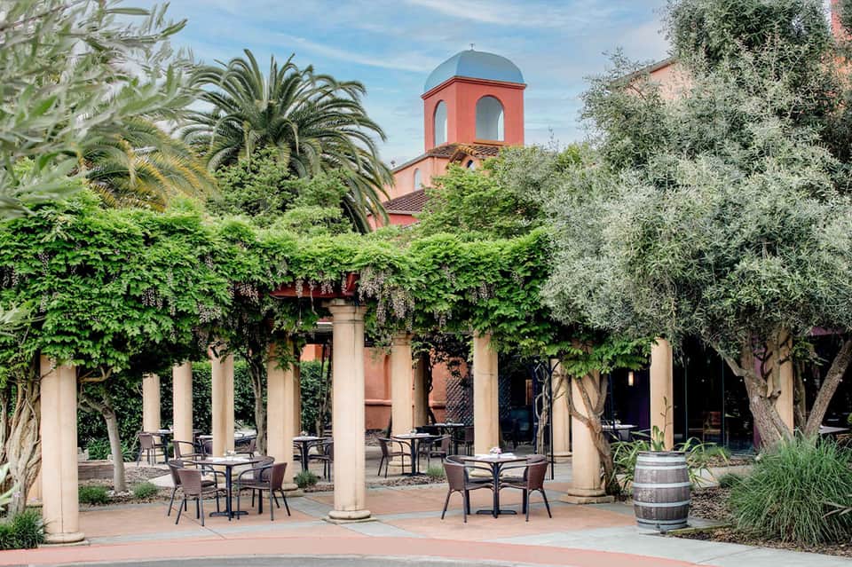 Lush courtyard with columns, Mediterranean architecture, olive trees, and red dome structure