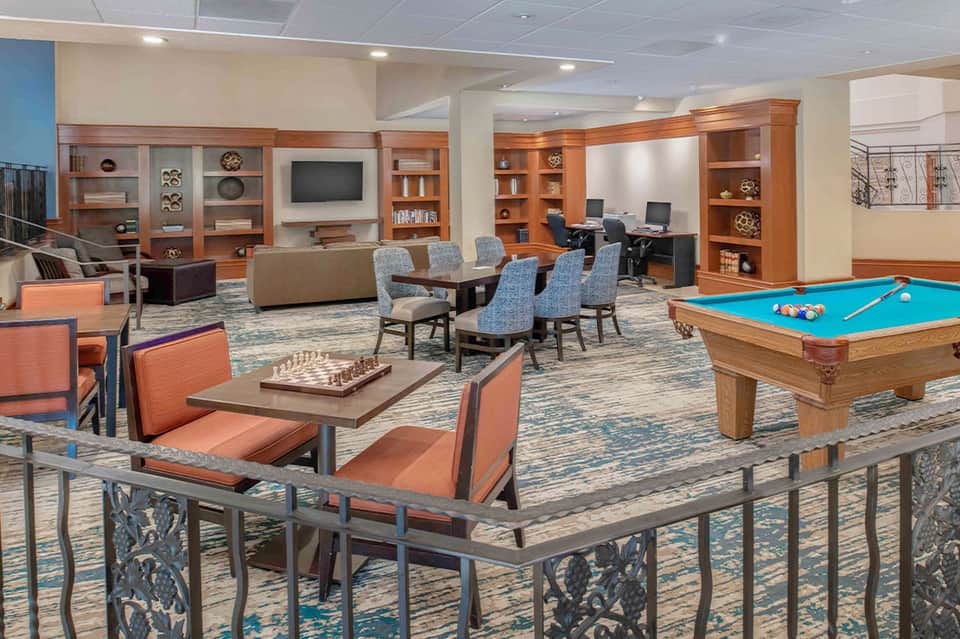 Hotel recreation room with pool table, seating areas, wooden cabinetry, and entertainment space