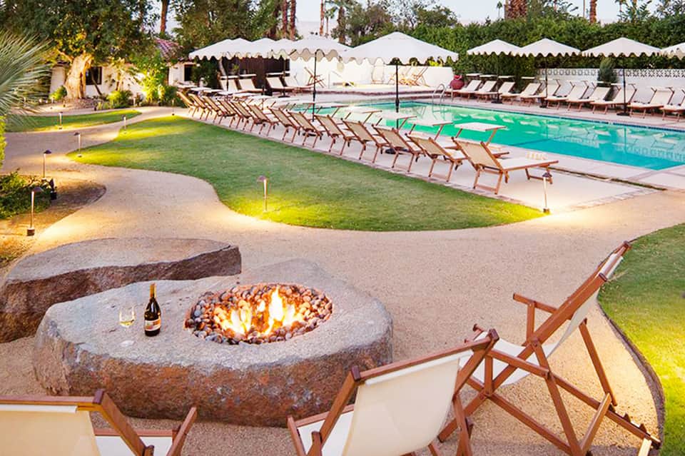 Outdoor pool area at dusk with fire pit, lounge chairs, white tent canopies, and palm trees