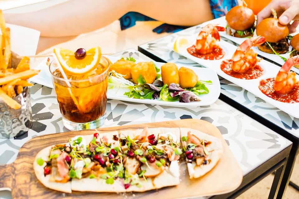 Colorful appetizers and cocktails displayed on white plates during outdoor resort dining event