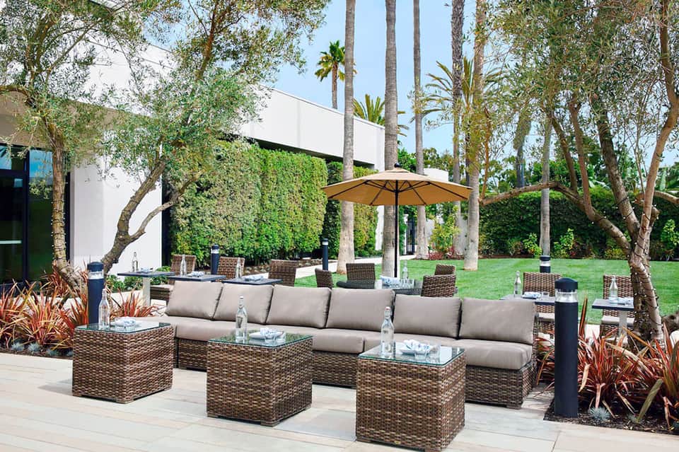 Contemporary outdoor lounge with rattan furniture, gray cushions, yellow umbrella, and manicured grounds