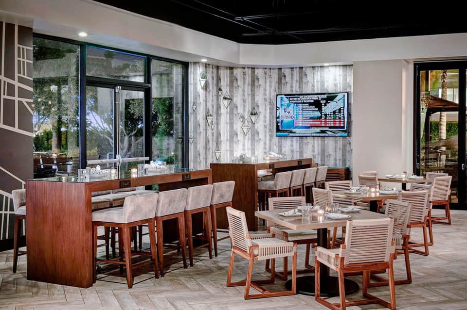 Modern resort bar and lounge area with wood furnishings, bar seating, and flat-screen TV