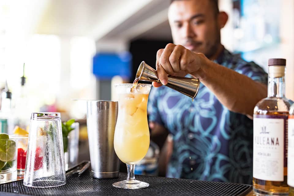 Bartender pouring cocktail into glass with citrus fruit and ice at resort bar
