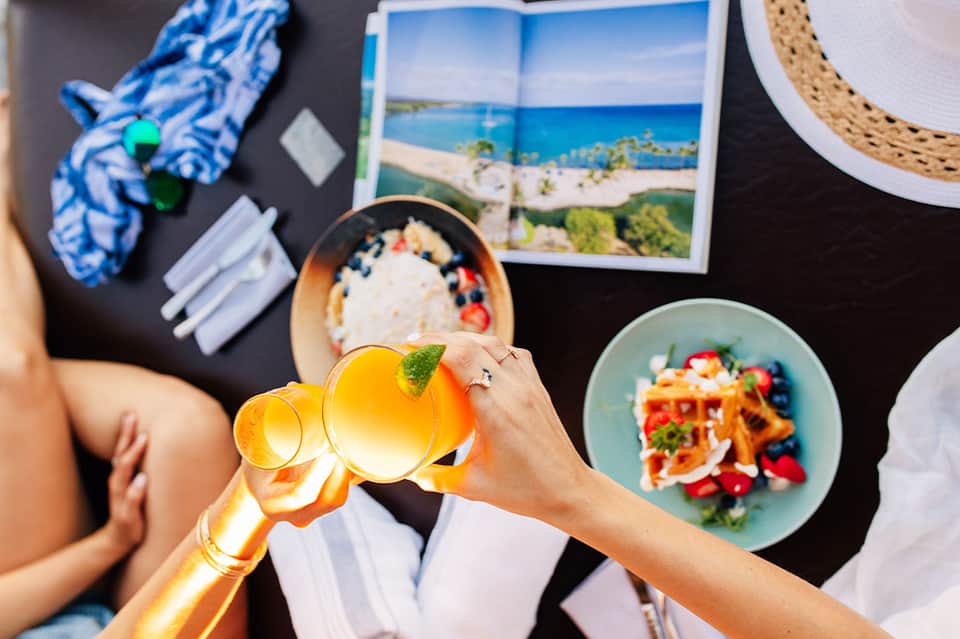 Beach vacation flatlay with tropical drinks, fresh food, travel photo, and sunscreen