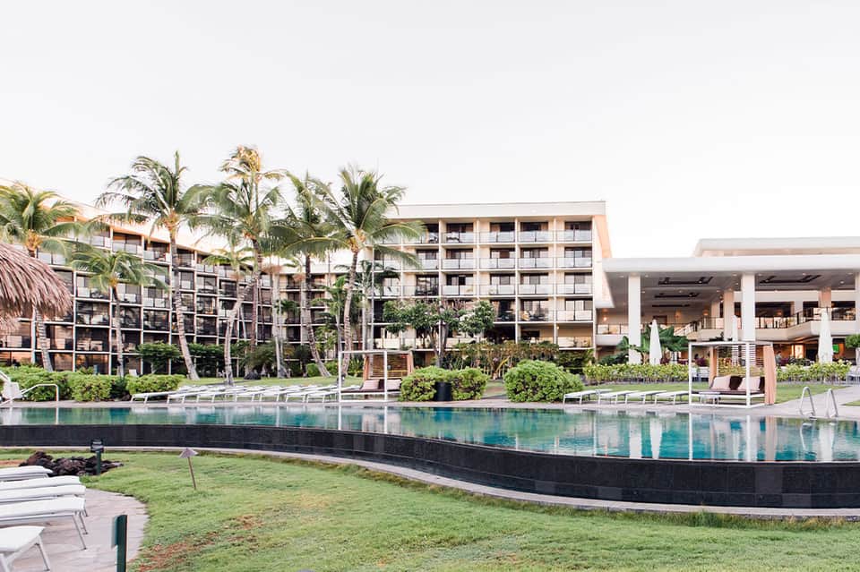 Modern resort property featuring sleek lap pool, contemporary architecture, palm trees, lounge areas, and multi-story hotel buildings
