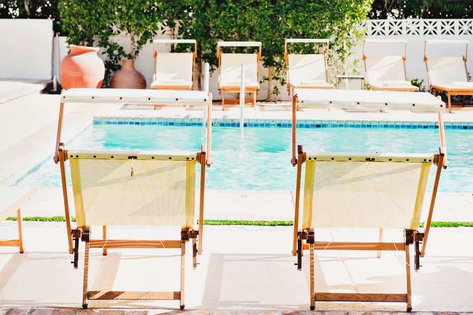 Two yellow and white deck chairs facing a turquoise swimming pool with lounge chairs in the background