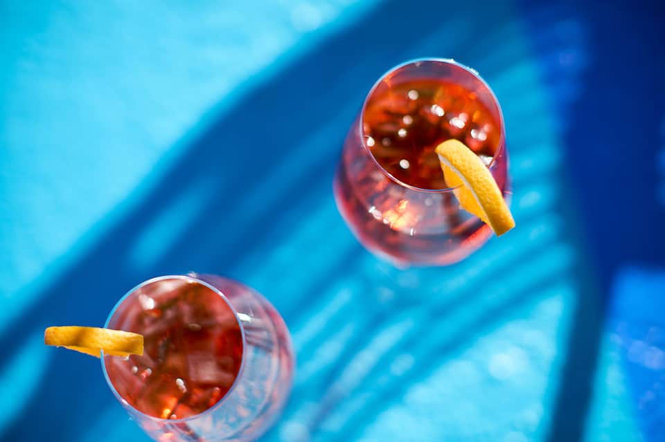 Two cocktails with ice and citrus garnish on turquoise poolside surface
