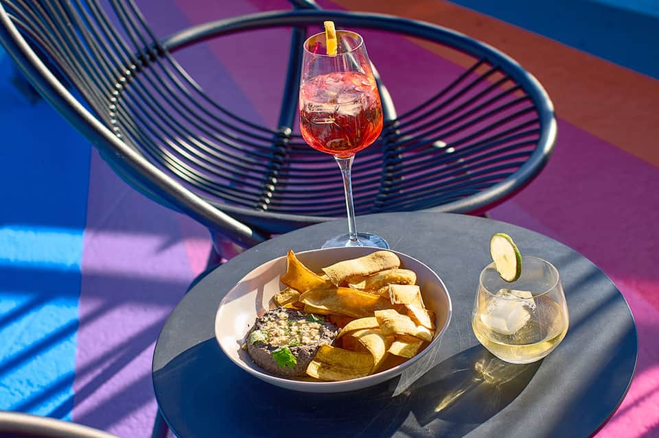 Colorful spiraling chair with plate of steak and fries, cocktail and water glass on dark table