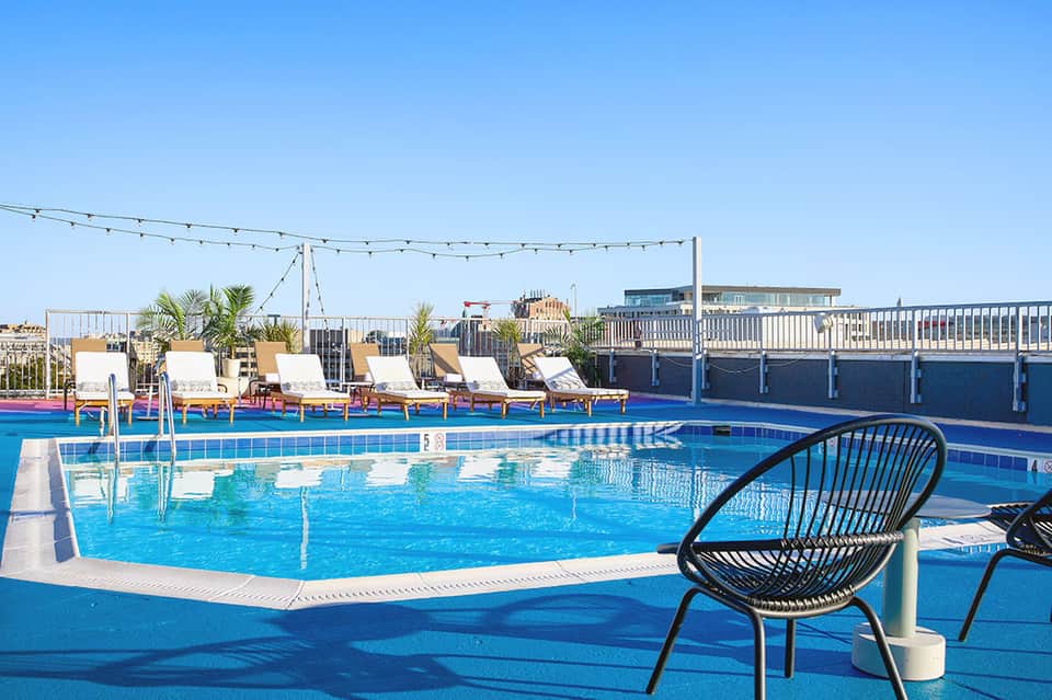 Rooftop pool with lounge chairs and string lights overlooking city skyline
