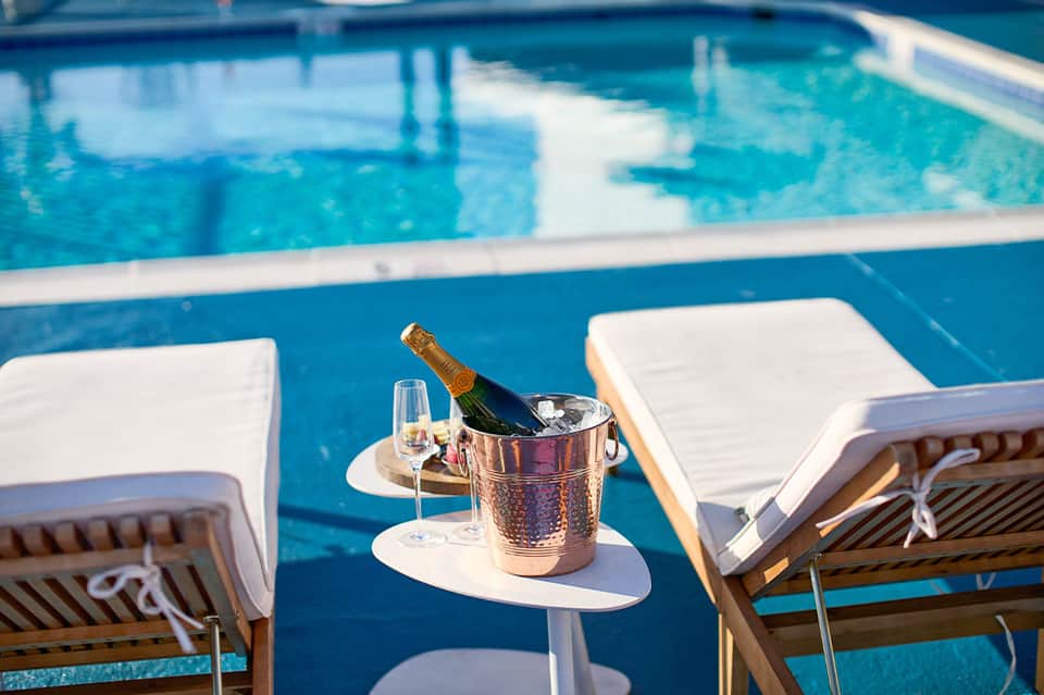 Champagne bottle chilling in ice bucket beside resort pool with white loungers