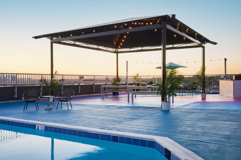 Rooftop pool deck at dusk with pergola, seating area, and panoramic city skyline views