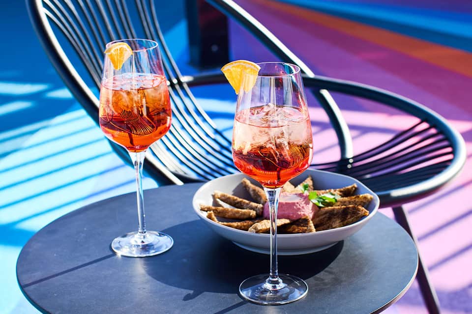 Two aperitif cocktails with appetizers on colorful striped lounge chair background