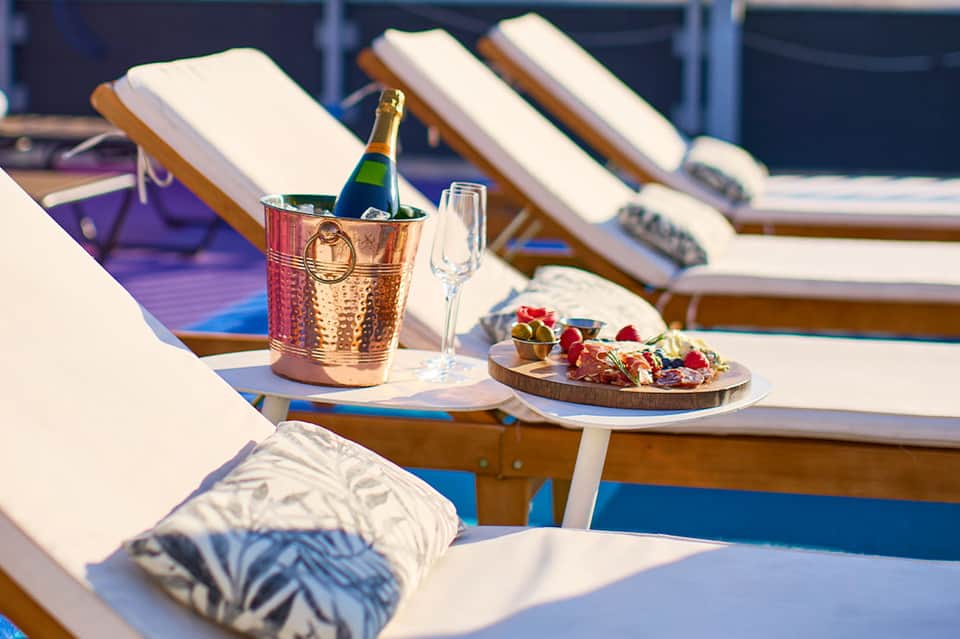 Champagne bottle in ice bucket and appetizer plate on lounger by resort pool