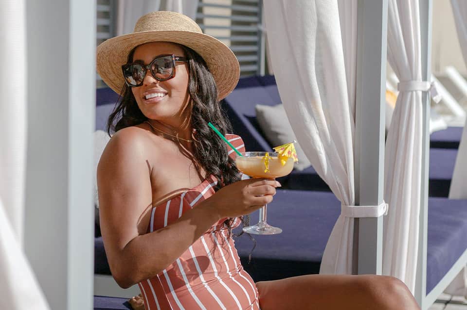 Woman in straw hat and sunglasses enjoying tropical cocktail on rooftop with city skyline backdrop